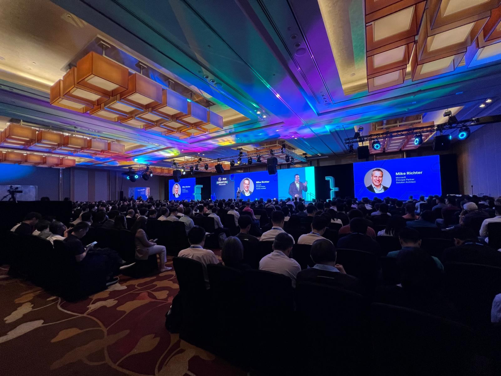 Mike Richter on stage at ElasticON Singapore 2026, name and Microsoft title displayed on three large screens above a packed audience.